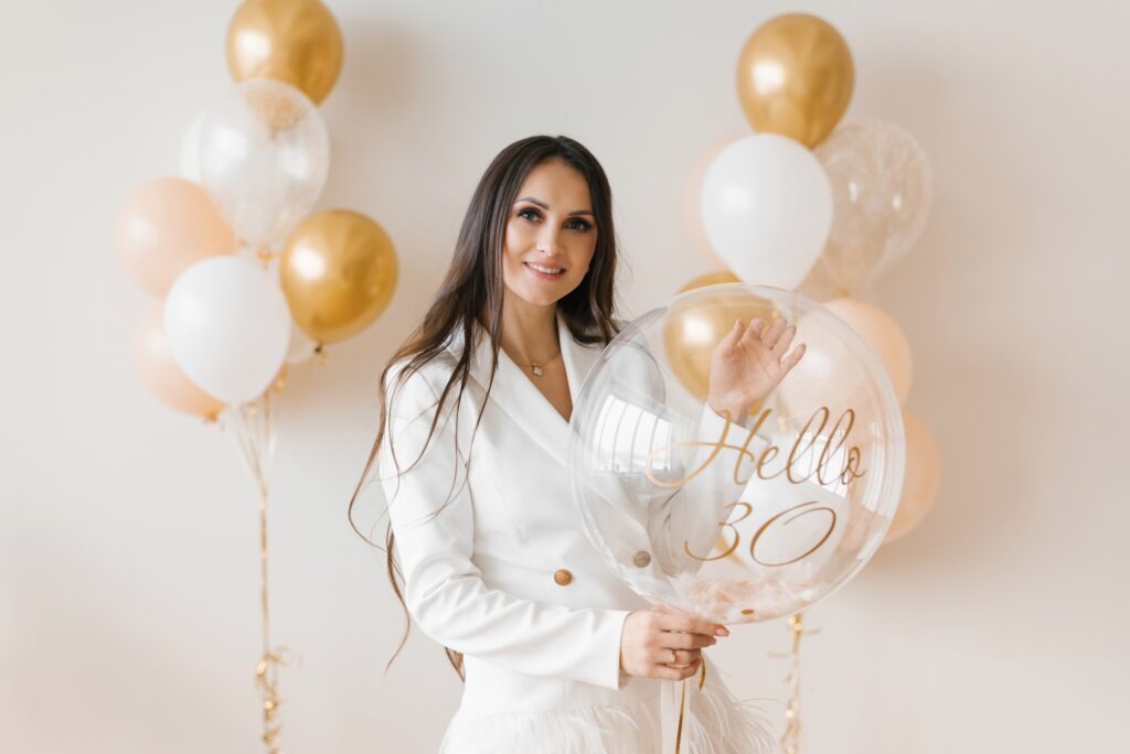 Woman Celebrating Anniversary Posing with Birthday Balloon Around Inflated Balloons